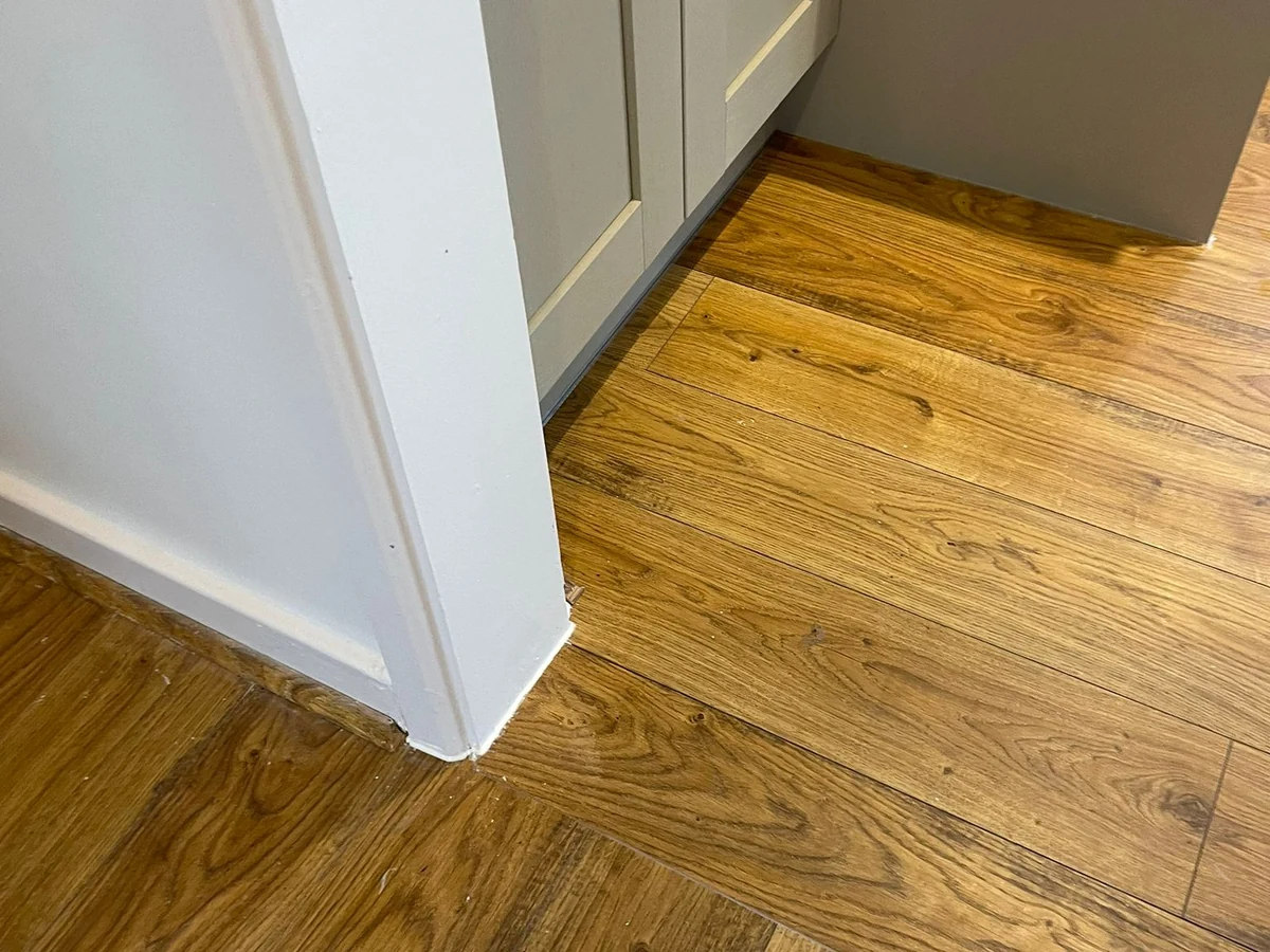 skirting-board-fitting-white-skirting-board-kitchen-cabinet-oak-floor-junction-swansea-daffodil-carpentry Wood-look flooring meeting white skirting and kitchen cabinets