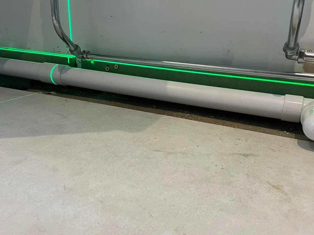 tiling-laser-level-under-sink-chrome-waste-pipes-pre-tile-swansea-daffodil-carpentry Laser level and waste pipes pre-tile during shower installation preparation in Swansea