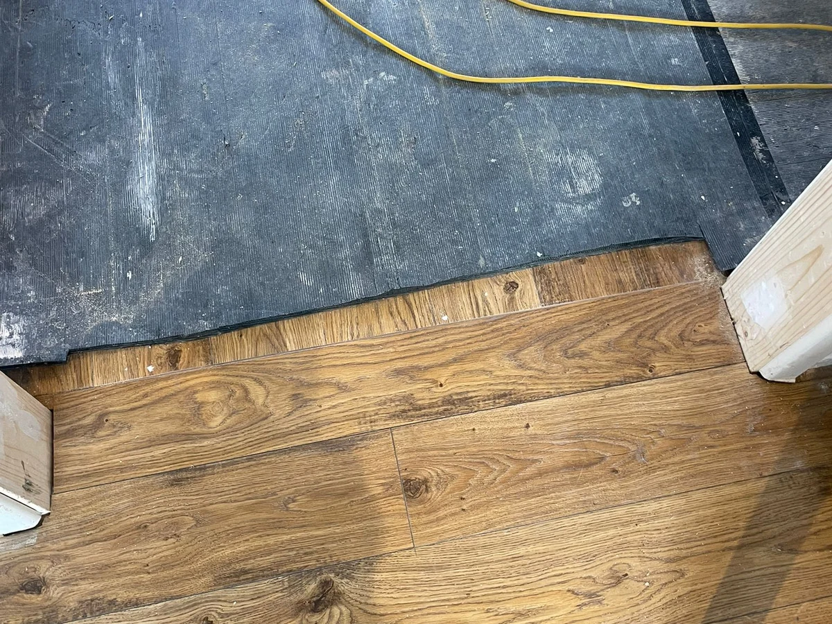 wood-floor-fitting-oak-boards-mid-lay-black-underlay-exposed-swansea-daffodil-carpentry Wood-look boards being fitted beside exposed underlay